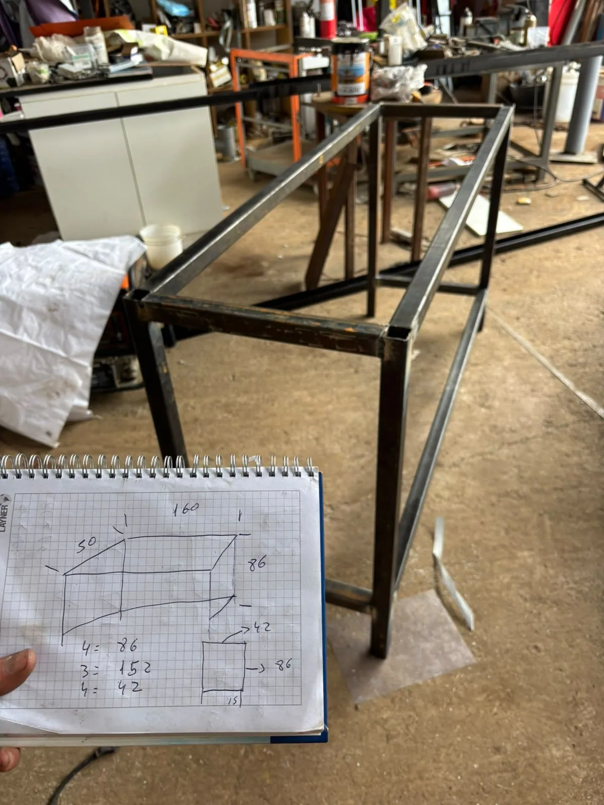 Estructura metálica en fabricación, junto a un dibujo con medidas.